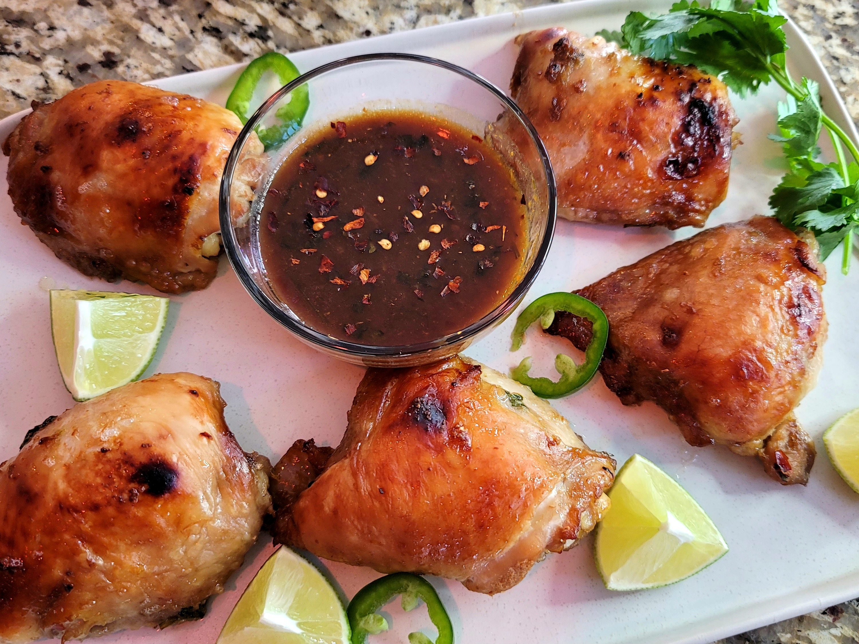 Golden-brown baked chicken thighs with crispy skin topped with fresh cilantro and lime zest on a white plate