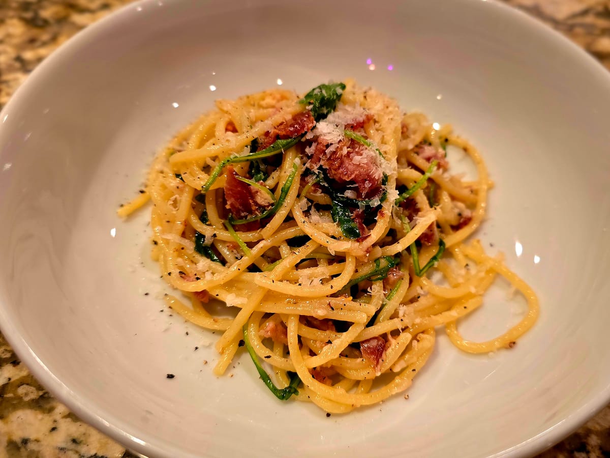 Rustic bacon arugula lemon spaghetti in a white bowl, topped with grated Parmesan and fresh peppery arugula, with crispy bacon pieces scattered throughout