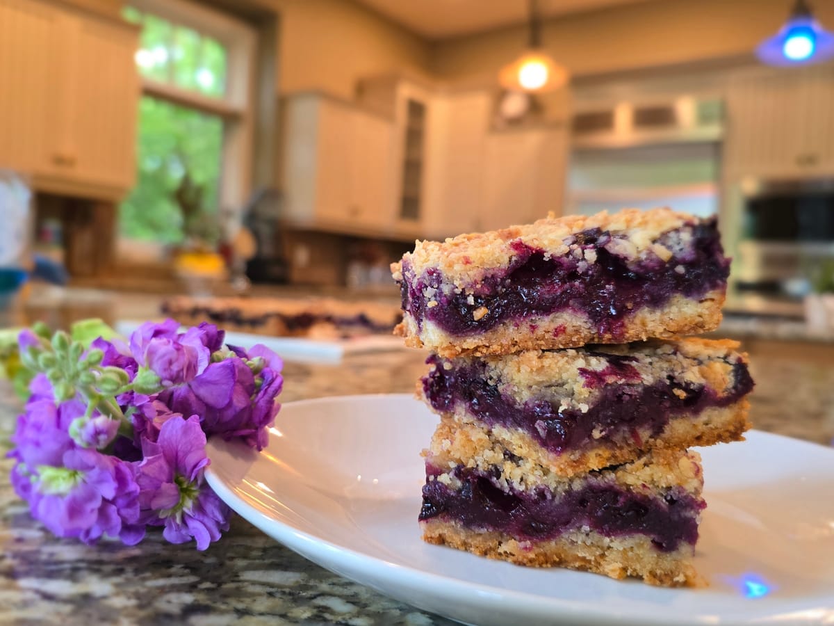Golden buttery blueberry crumble bars with fresh blueberries, flaky crumb topping, and lemon zest on parchment paper