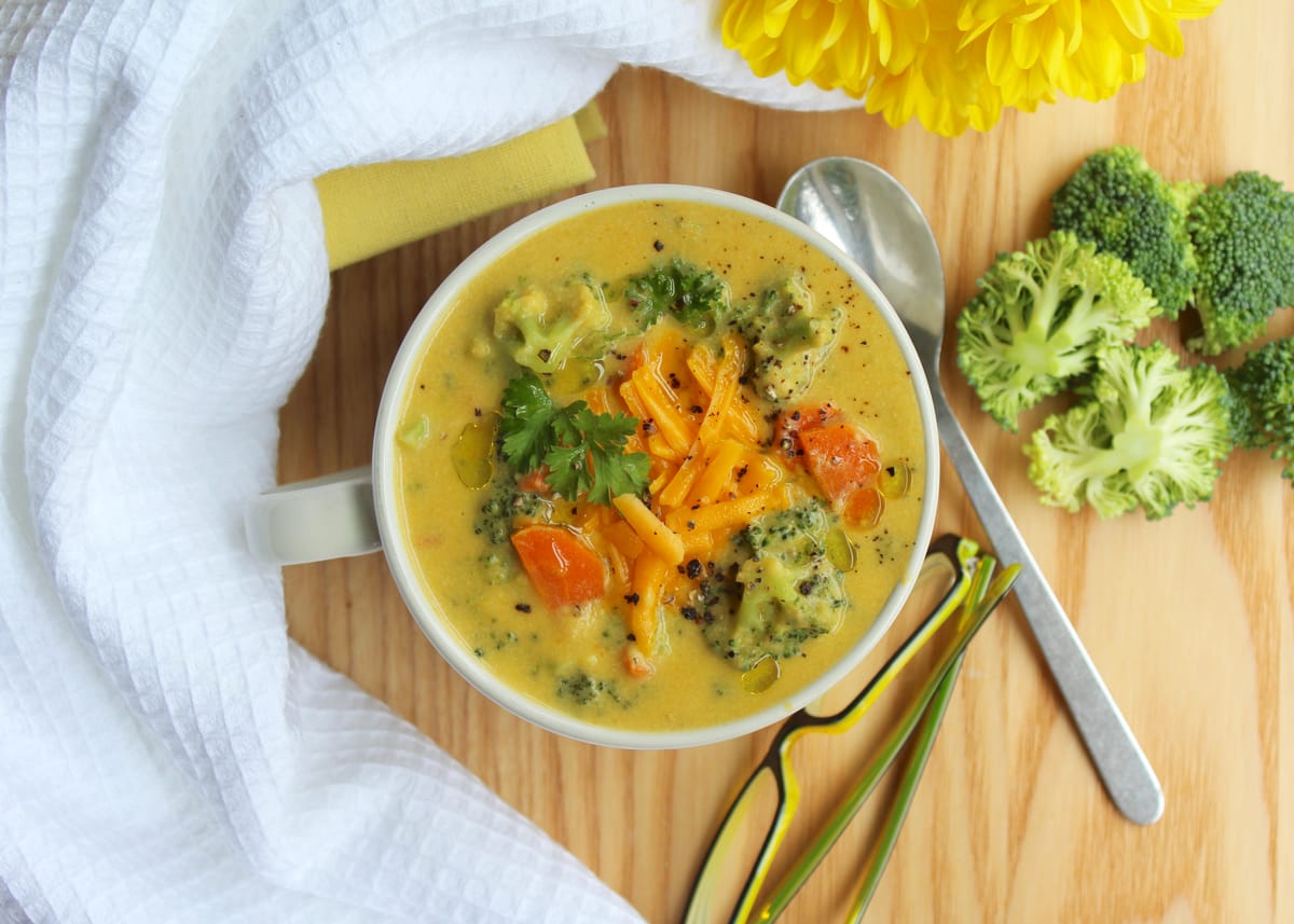 Creamy broccoli cheese soup in a white bowl with fresh broccoli florets and melted cheese garnish