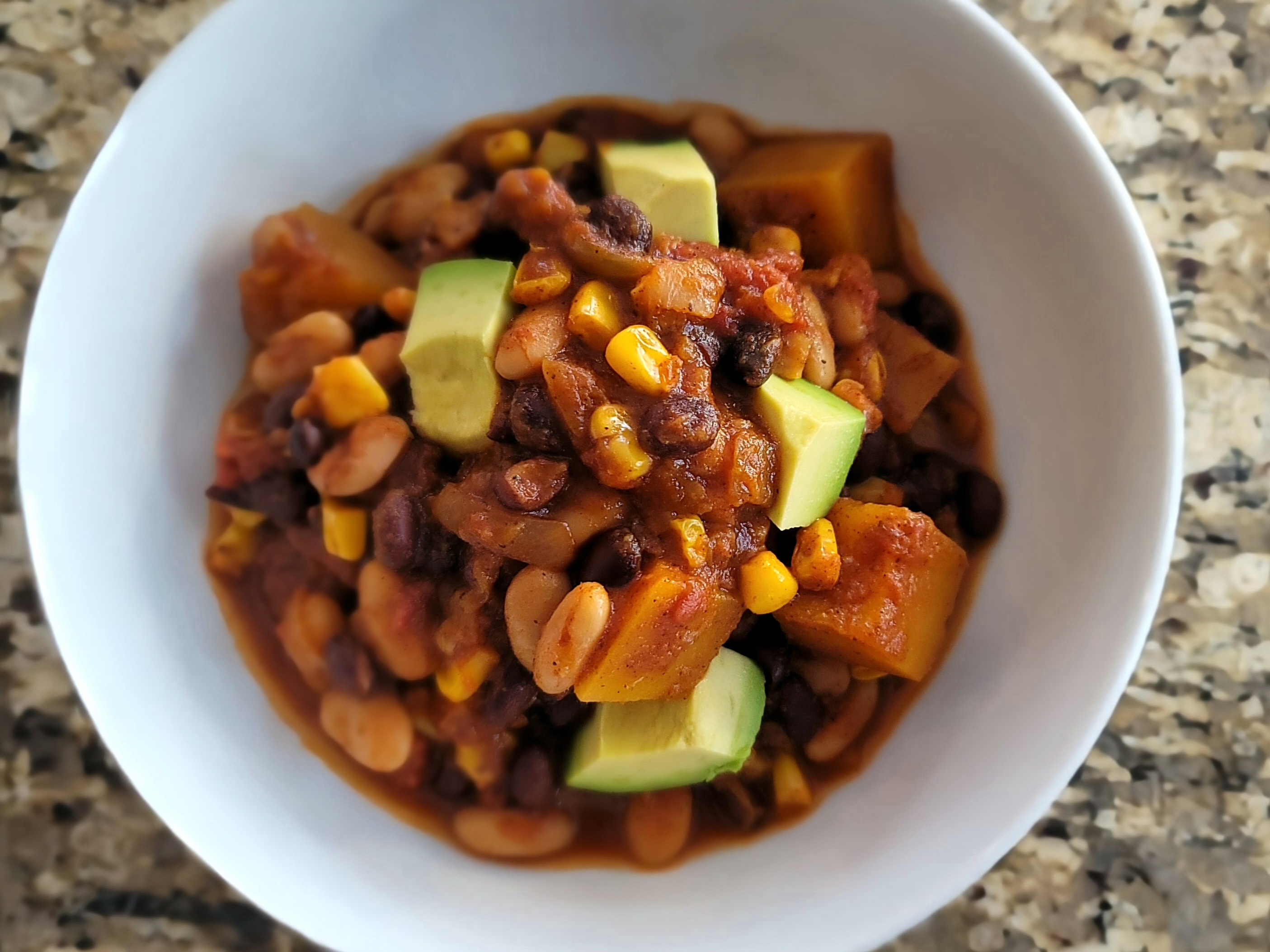 Bowl of butternut squash chili topped with diced onions, served with crusty bread on a wooden table
