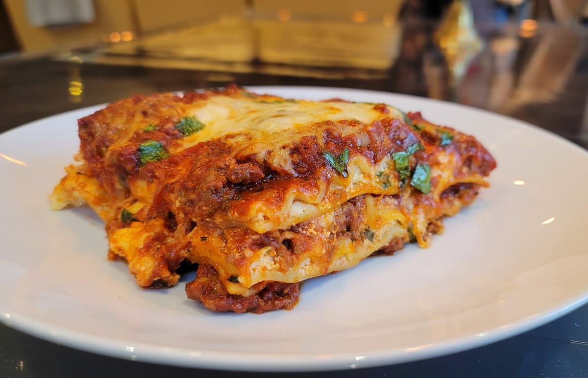 Classic lasagna with layers of melted cheese, rich meat sauce, and pasta visible on a white plate with fresh basil garnish