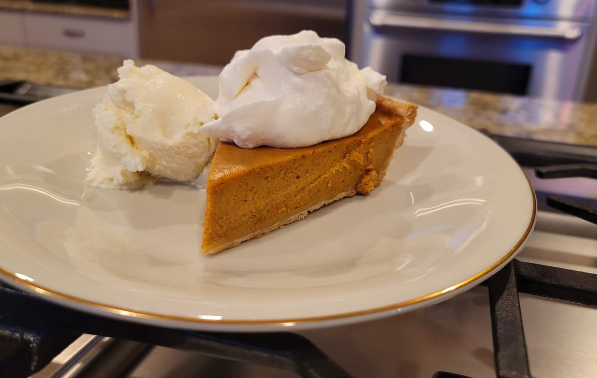 Golden-brown classic pumpkin pie with a fluted crimped crust edge, showing creamy pumpkin filling inside on a white plate