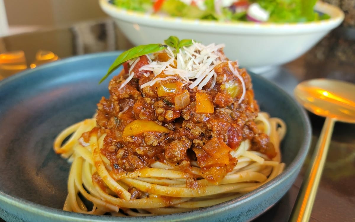 Rich, glossy meat sauce with visible ground beef, sausage, mushrooms, peppers, and onions in a large pot