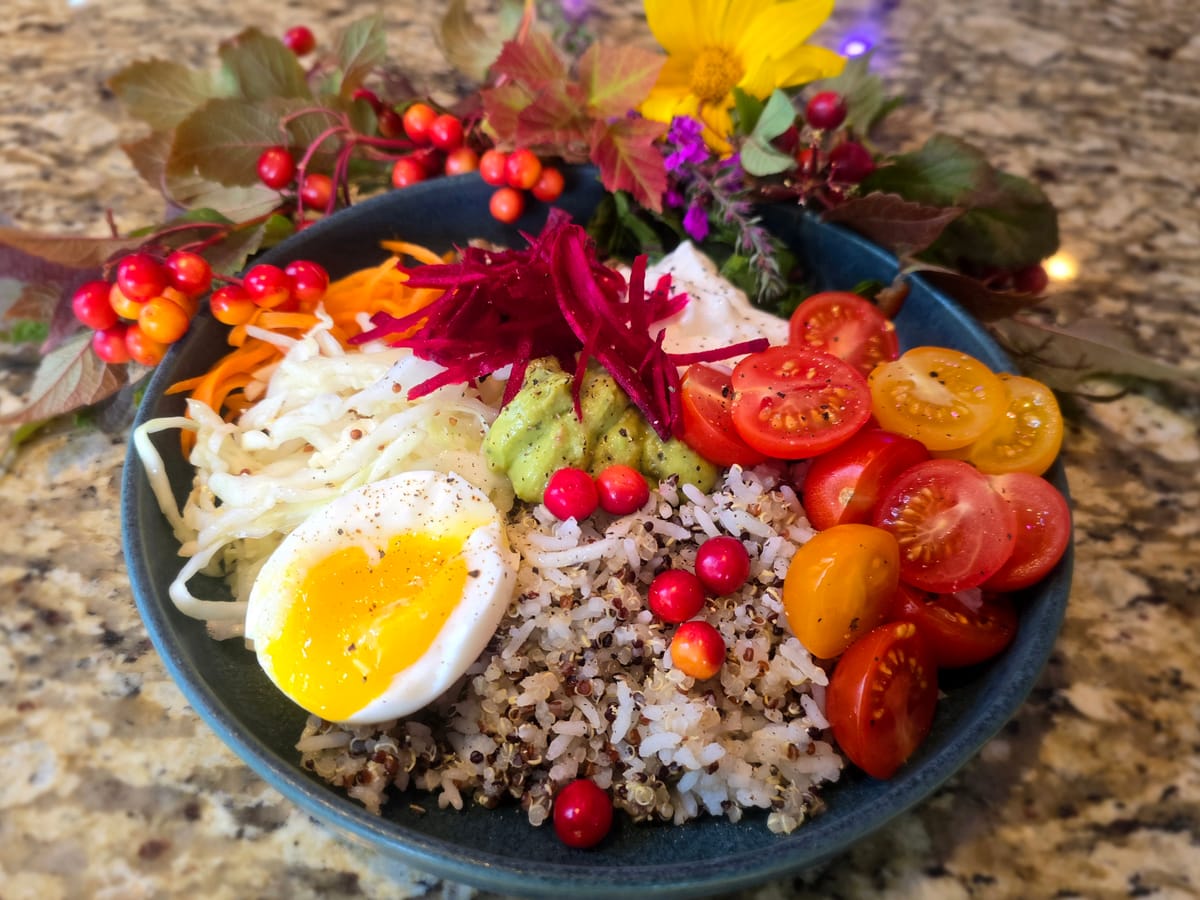 Colorful power bowl with quinoa, brown rice, roasted beets, fresh greens, cucumber, carrots, and grilled chicken breast topped with yogurt sauce