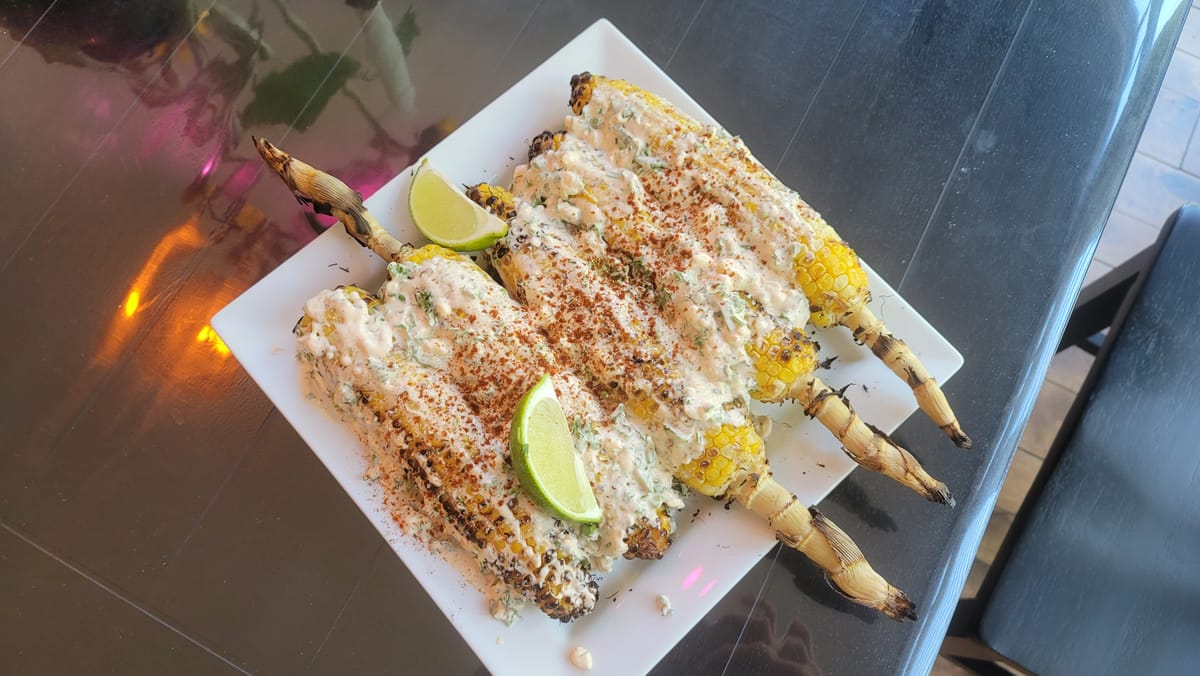 Grilled Mexican street corn coated with creamy mayo, crumbled feta cheese, cilantro, and chili powder on a white plate with lime wedges