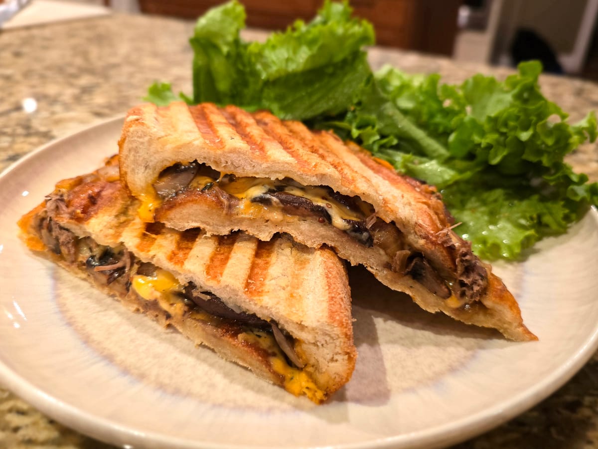 Golden-brown mushroom melt panini with melted Gouda and cheddar cheese, caramelized onions, and fresh mushrooms on a plate