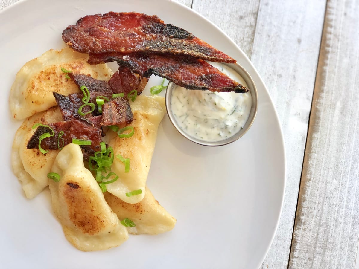 Golden-brown perogies on a white plate topped with caramelized onions and sour cream, with fresh chives garnish