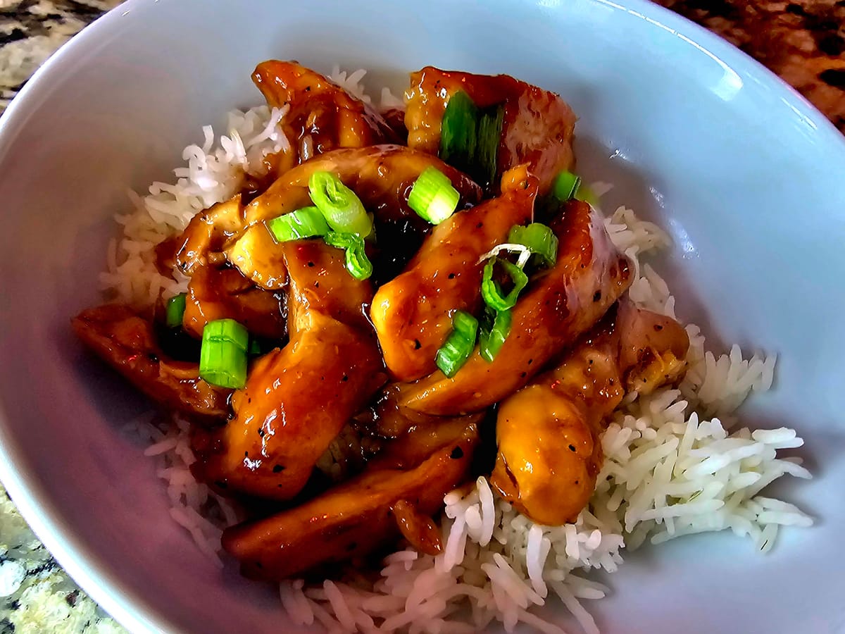 Golden pan-seared chicken thighs coated in glossy teriyaki sauce with garlic and sesame garnish in a skillet