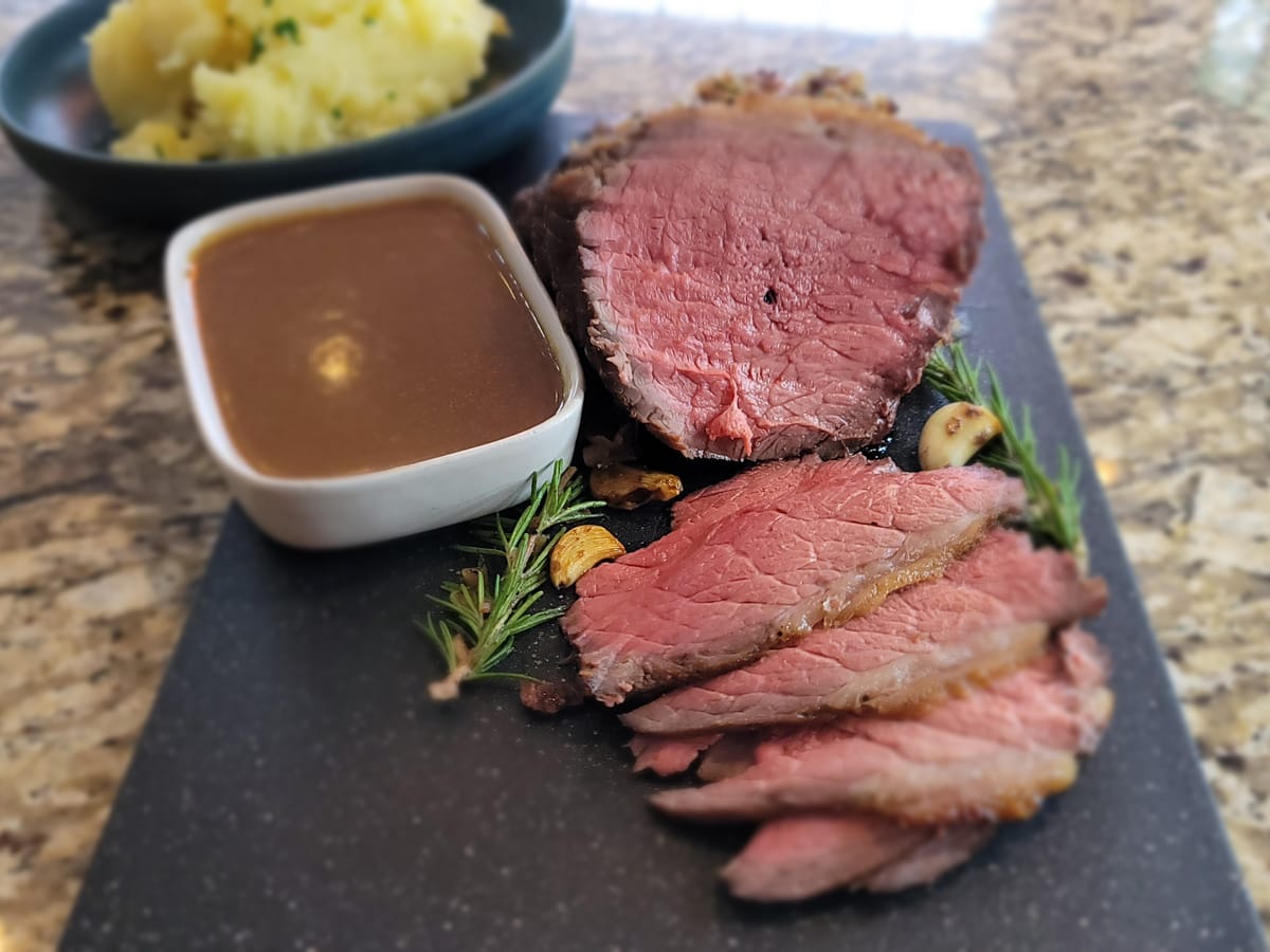 Perfectly cooked roast beef with golden brown crust, sliced to show pink medium-rare center, served on a white plate