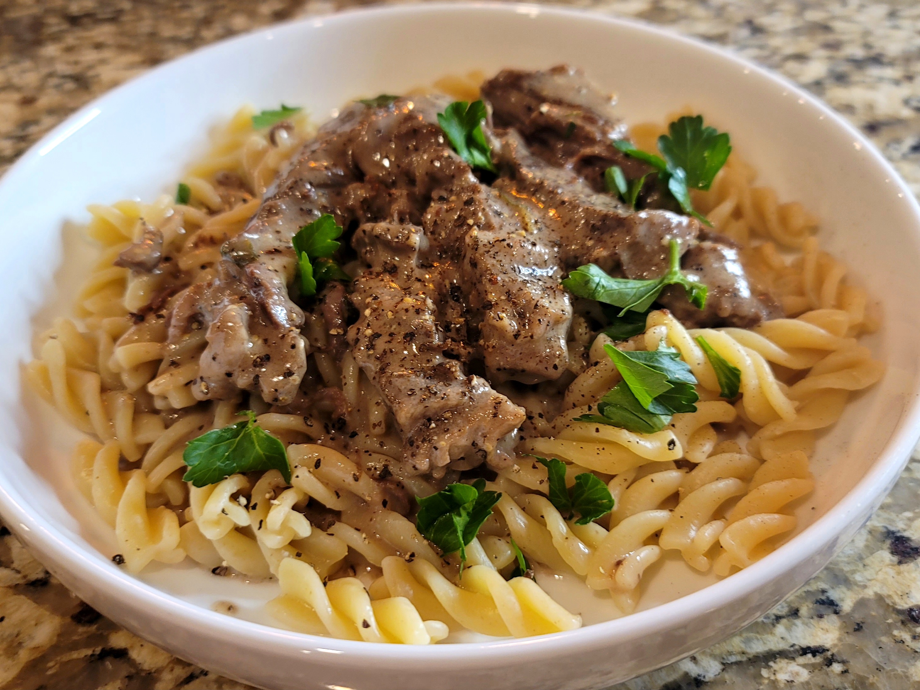 Tender fall-apart beef stroganoff with creamy sauce, mushrooms, and onions in a white bowl