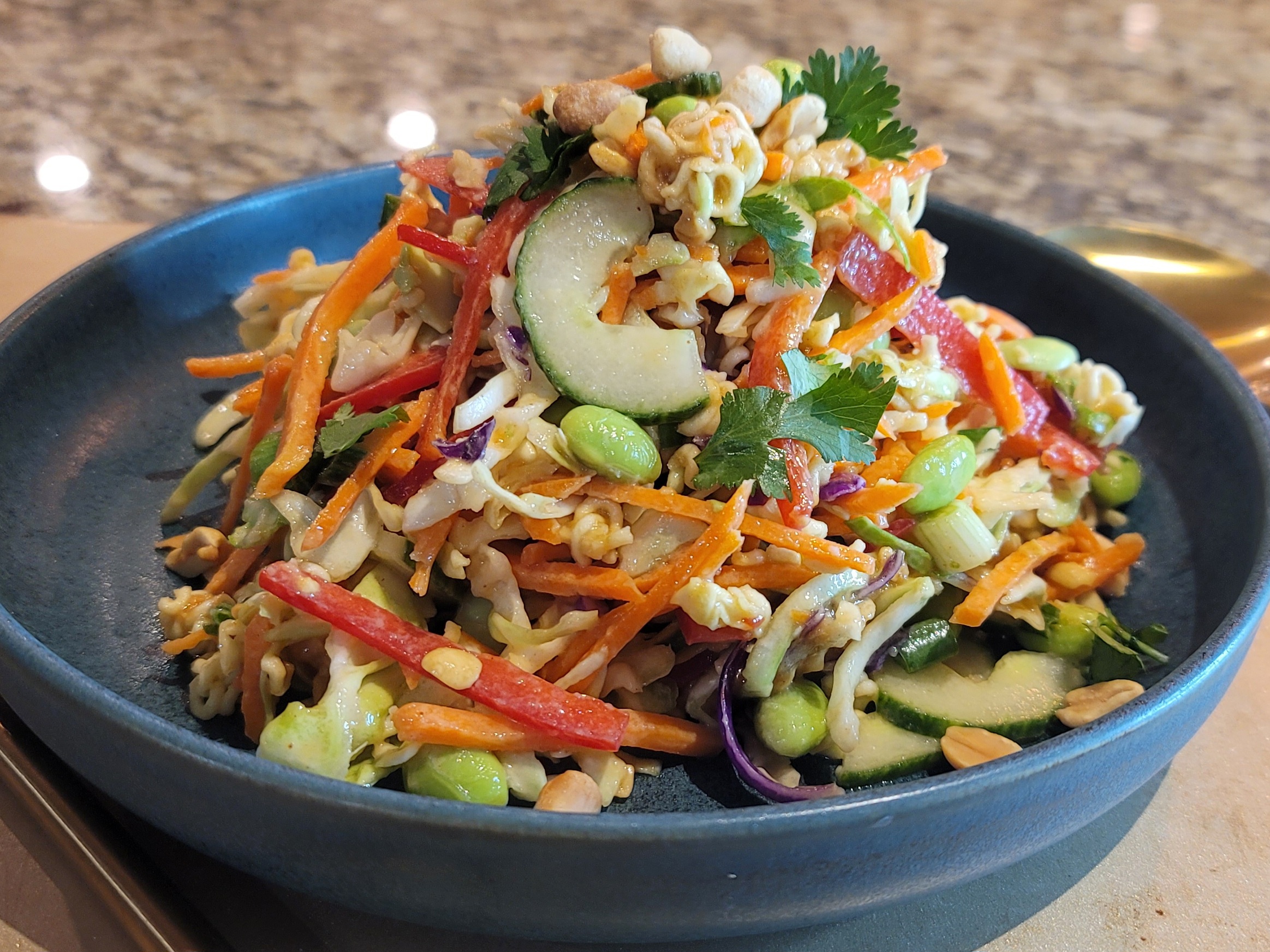 Thai crunch salad with shredded cabbage, colorful bell peppers, edamame, crispy ramen noodles, and cashews in a white bowl