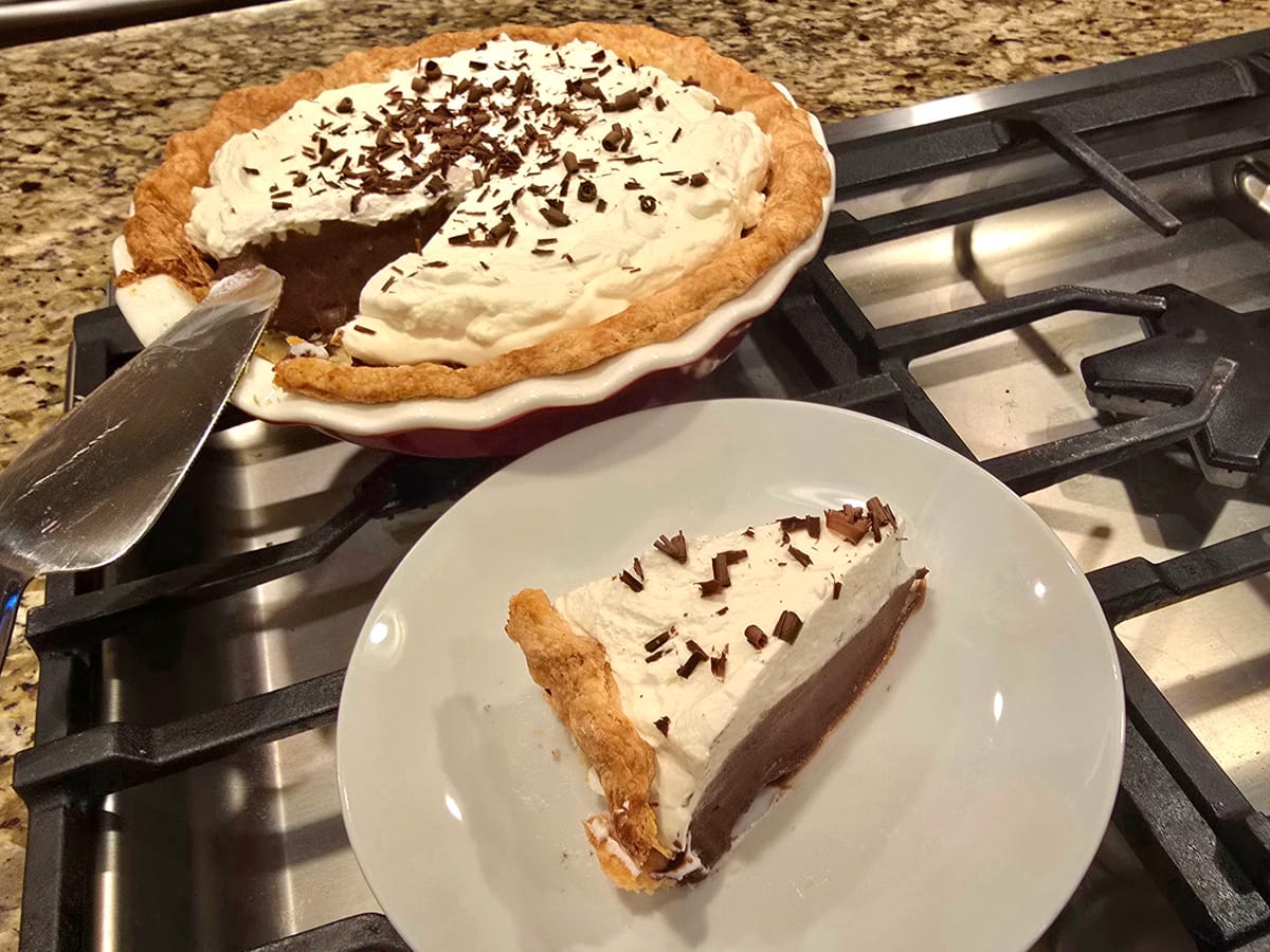 Ultimate chocolate cream pie with golden flaky crust, silky chocolate filling, and fluffy whipped cream topping on a white plate