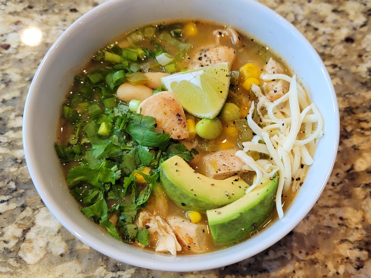 White chicken chili in a bowl with diced chicken, white beans, and poblano peppers garnished with cilantro