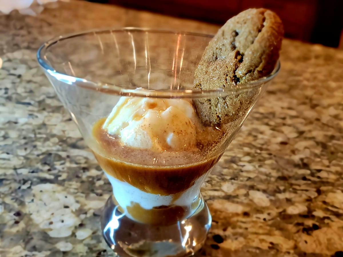 A scoop of vanilla ice cream in a glass with hot espresso being poured over it, creating a creamy coffee drink