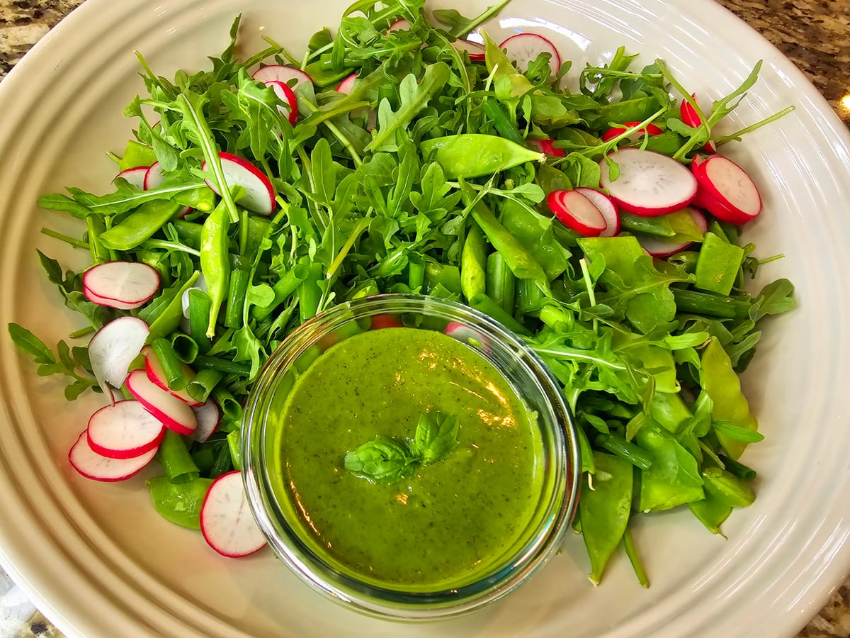 Vibrant arugula salad with sliced radishes and green onions, dressed in honey basil vinaigrette, on a white plate
