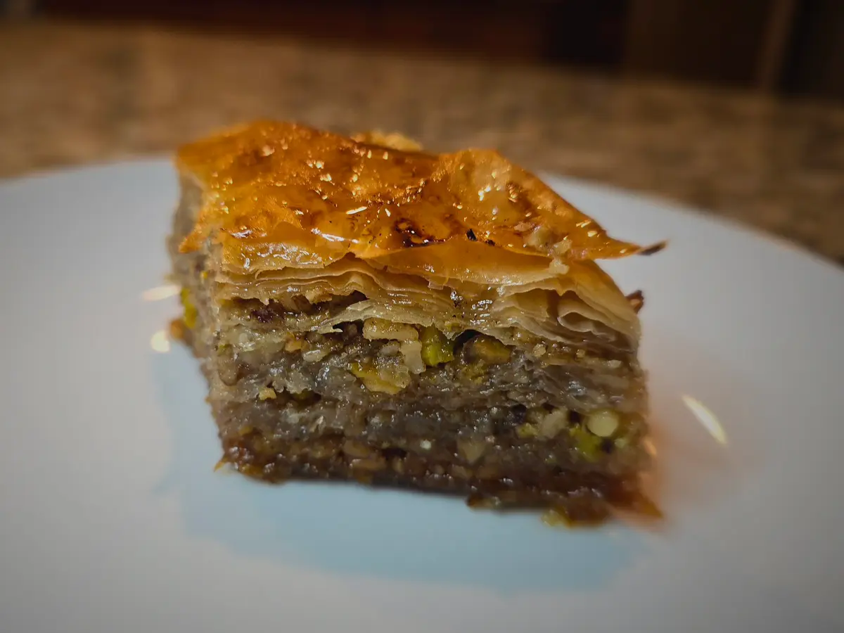 Golden crispy baklava pieces stacked together with honey dripping, showing layers of phyllo dough and chopped walnuts
