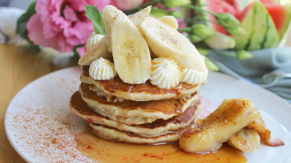 Stack of golden fluffy banana pancakes topped with butter and syrup on a white plate