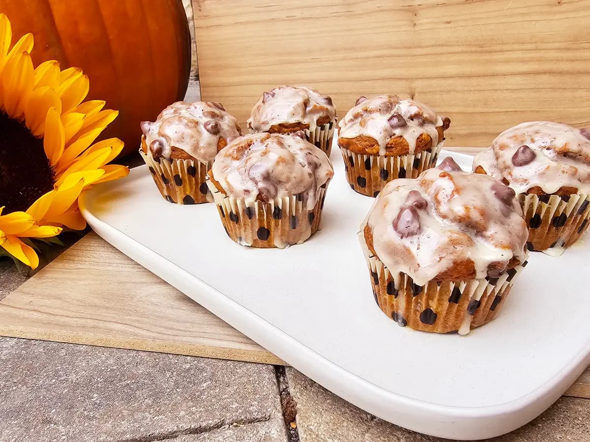 Banana pumpkin muffins with brown butter maple glaze on a white plate, topped with glossy golden glaze and autumn spices