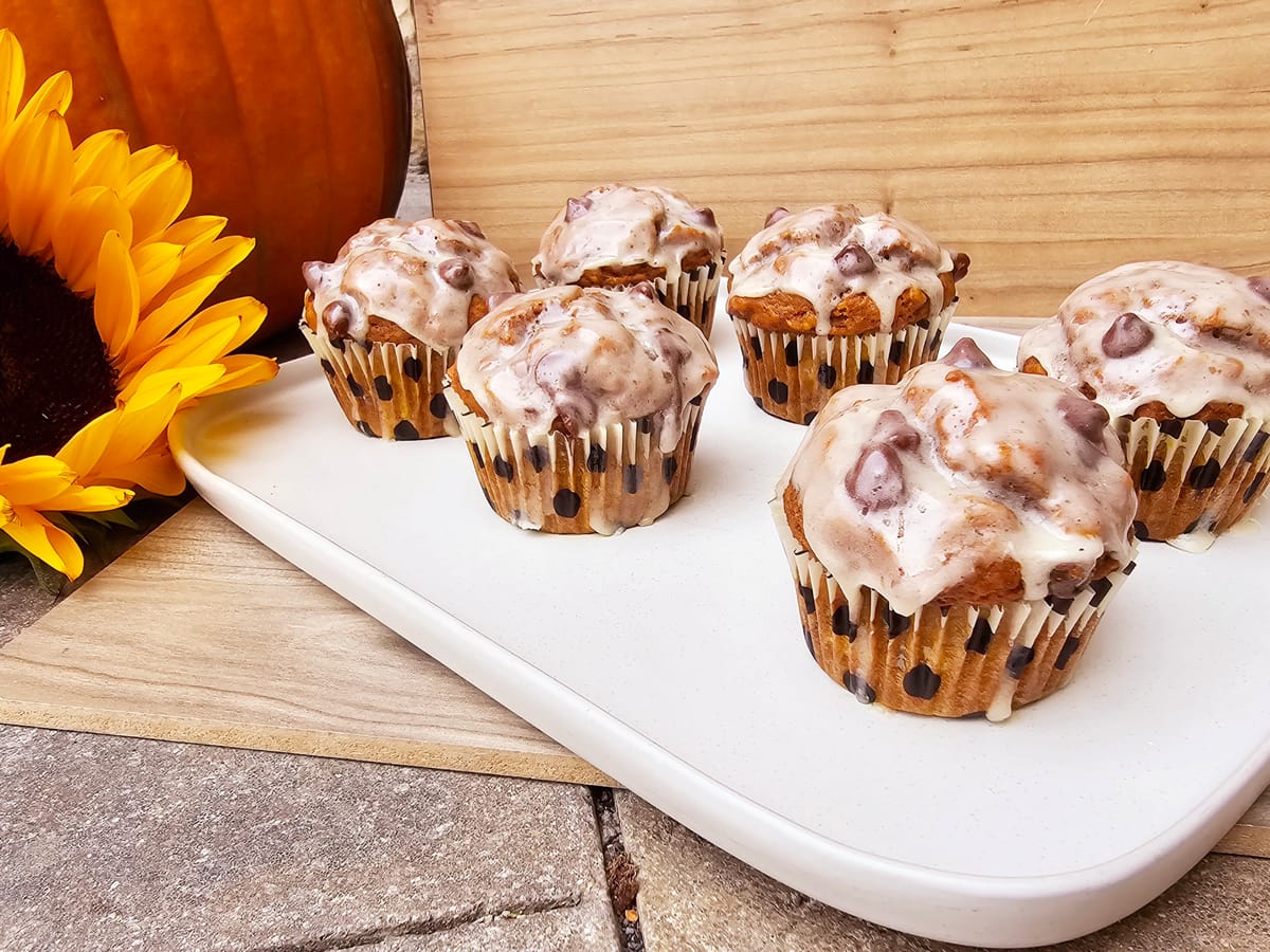 Banana pumpkin muffins with brown butter maple glaze on a white plate, topped with glossy golden glaze and autumn spices