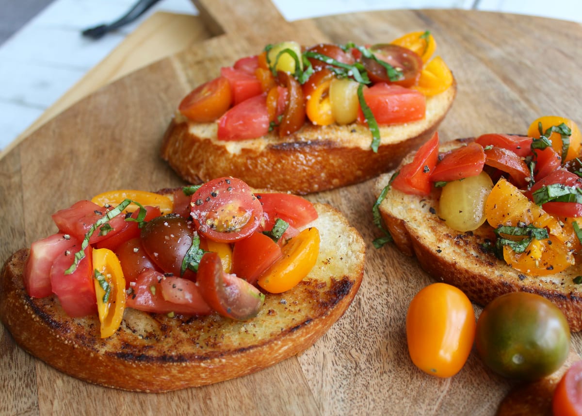 Golden toasted bruschetta slices topped with fresh tomato and basil mixture on a white plate