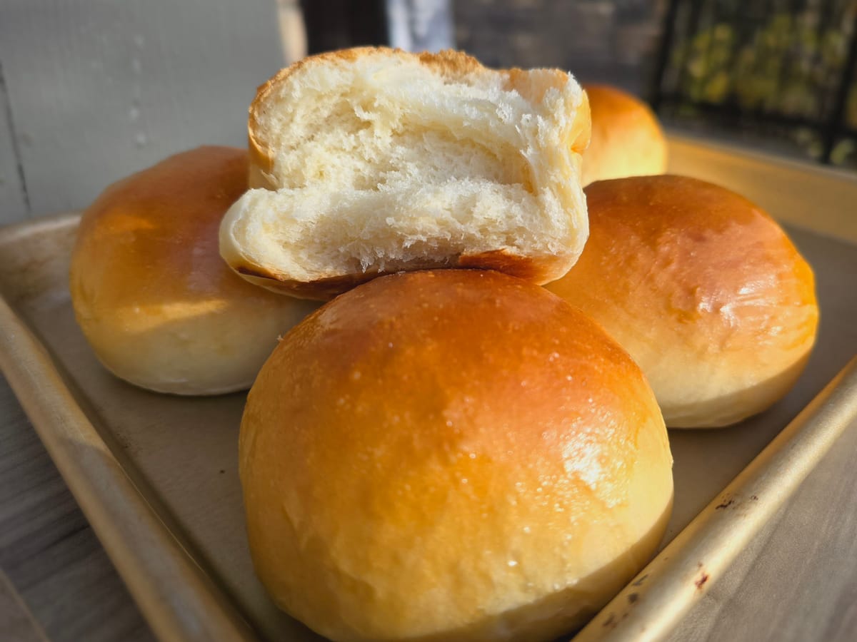 Golden-brown Canadian prairie dinner buns stacked in a basket, showing their soft, fluffy texture and glossy surface