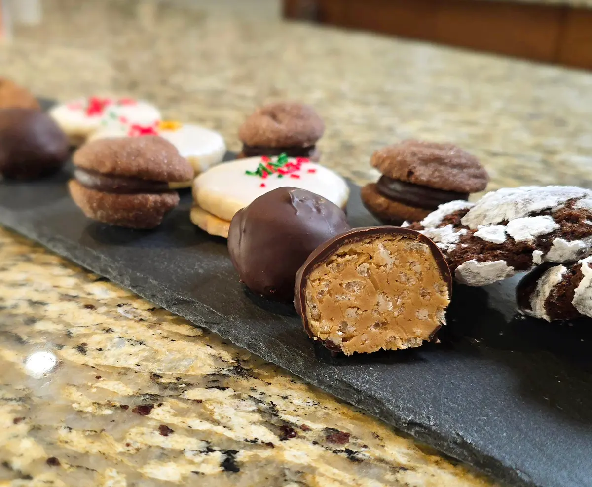 Golden peanut butter rice crispy chocolate balls stacked on a white plate, coated in rich dark chocolate with a glimpse of the crunchy peanut butter center