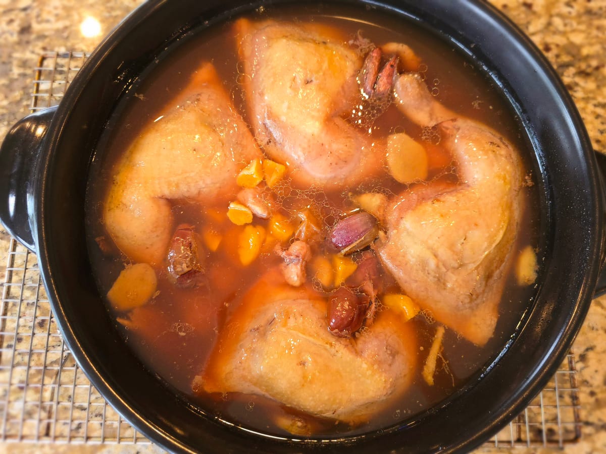 Golden simmering Chinese ginger chicken tonic soup with red dates and goji berries in a traditional donabe clay pot