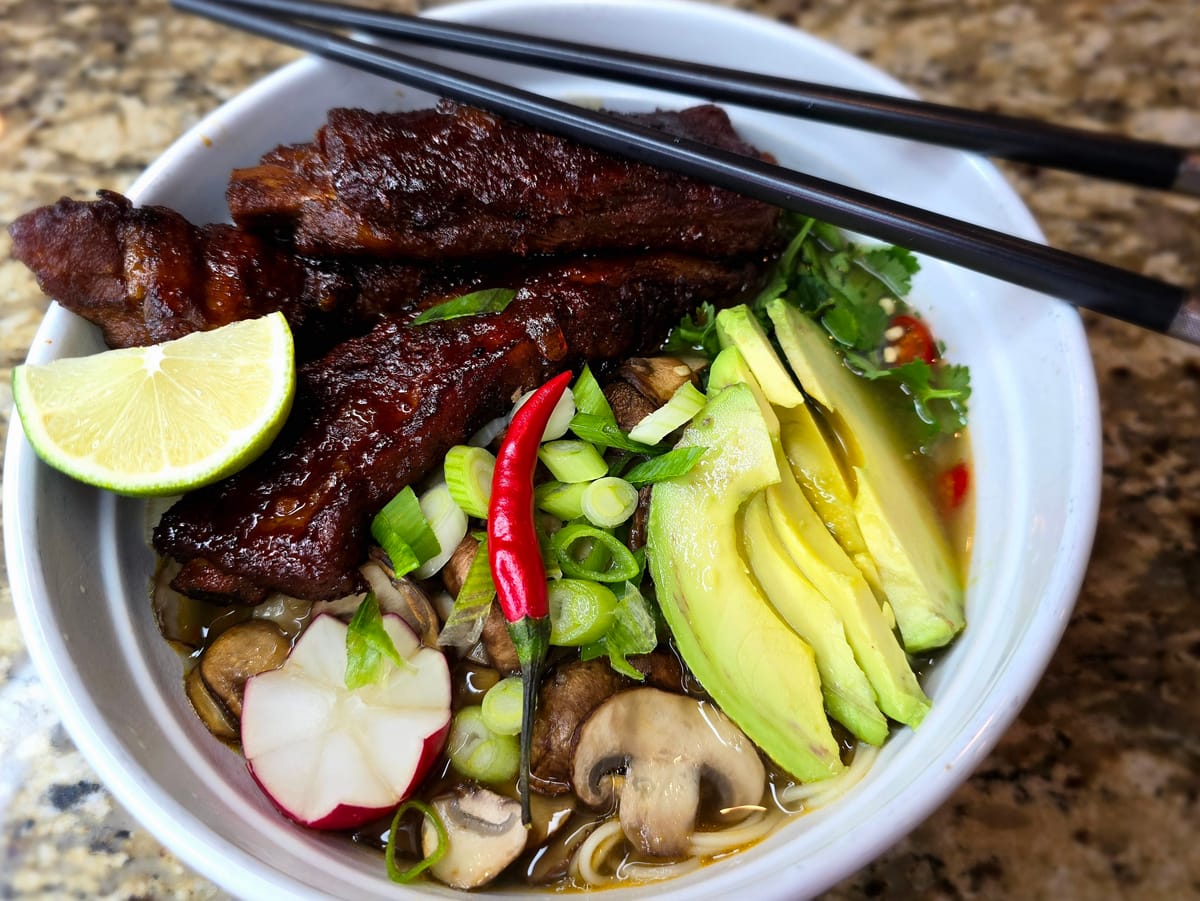 Bowl of Chinese noodle soup with tender braised pork ribs in sriracha honey broth, garnished with green onions