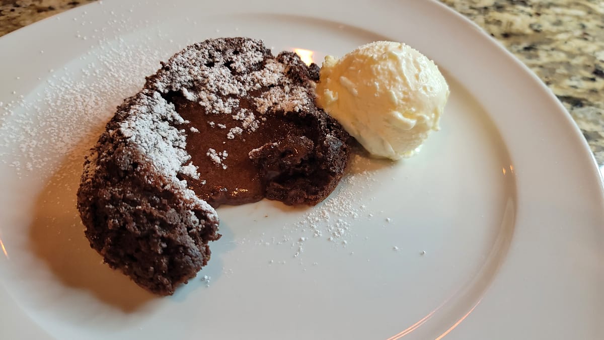 Golden-brown chocolate molten lava cake with warm gooey chocolate center oozing out, served on a white plate with powdered sugar and fresh raspberries