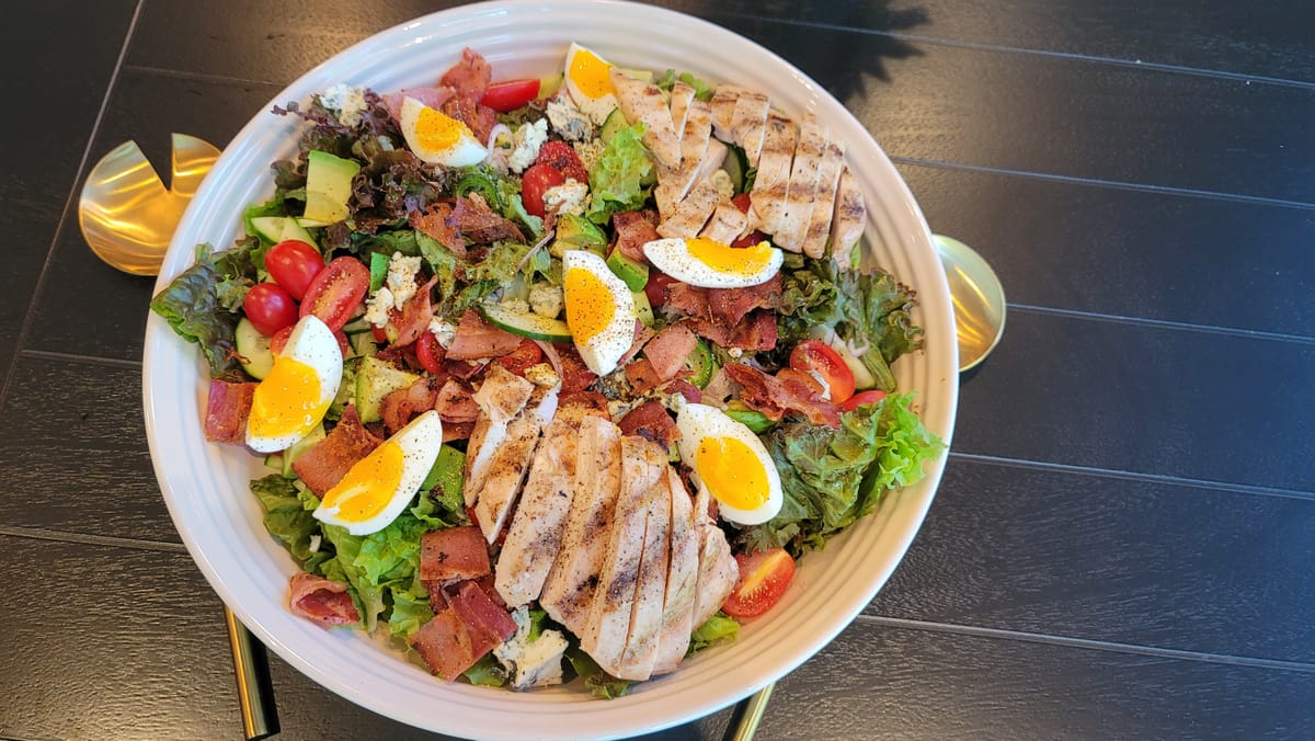 Cobb salad with crispy bacon, sliced chicken, avocado, hard-boiled eggs, blue cheese, and fresh greens on a white plate