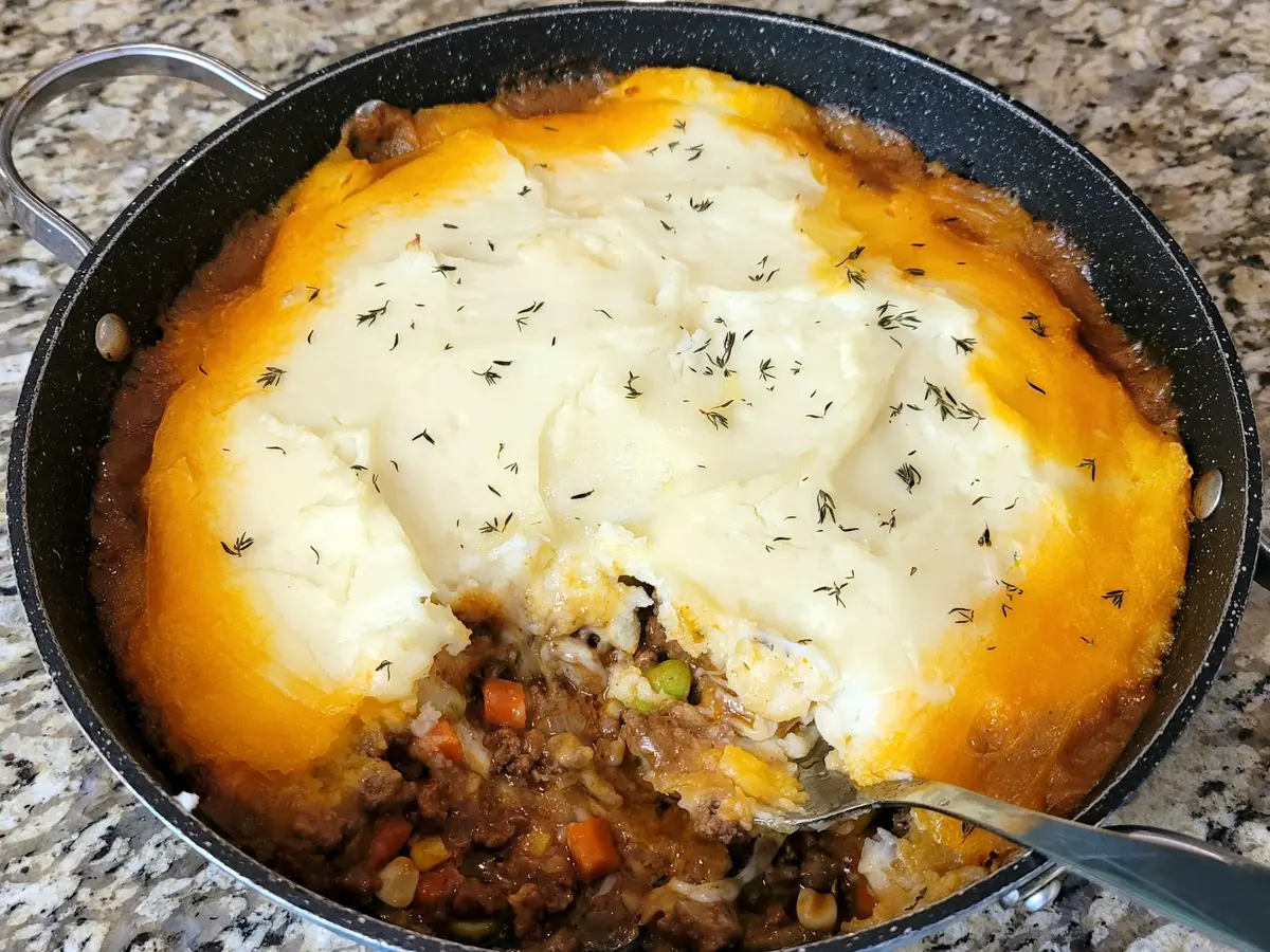 Shepherd's pie with melted cheese curds topping over creamy mashed potatoes and ground beef filling in a baking dish