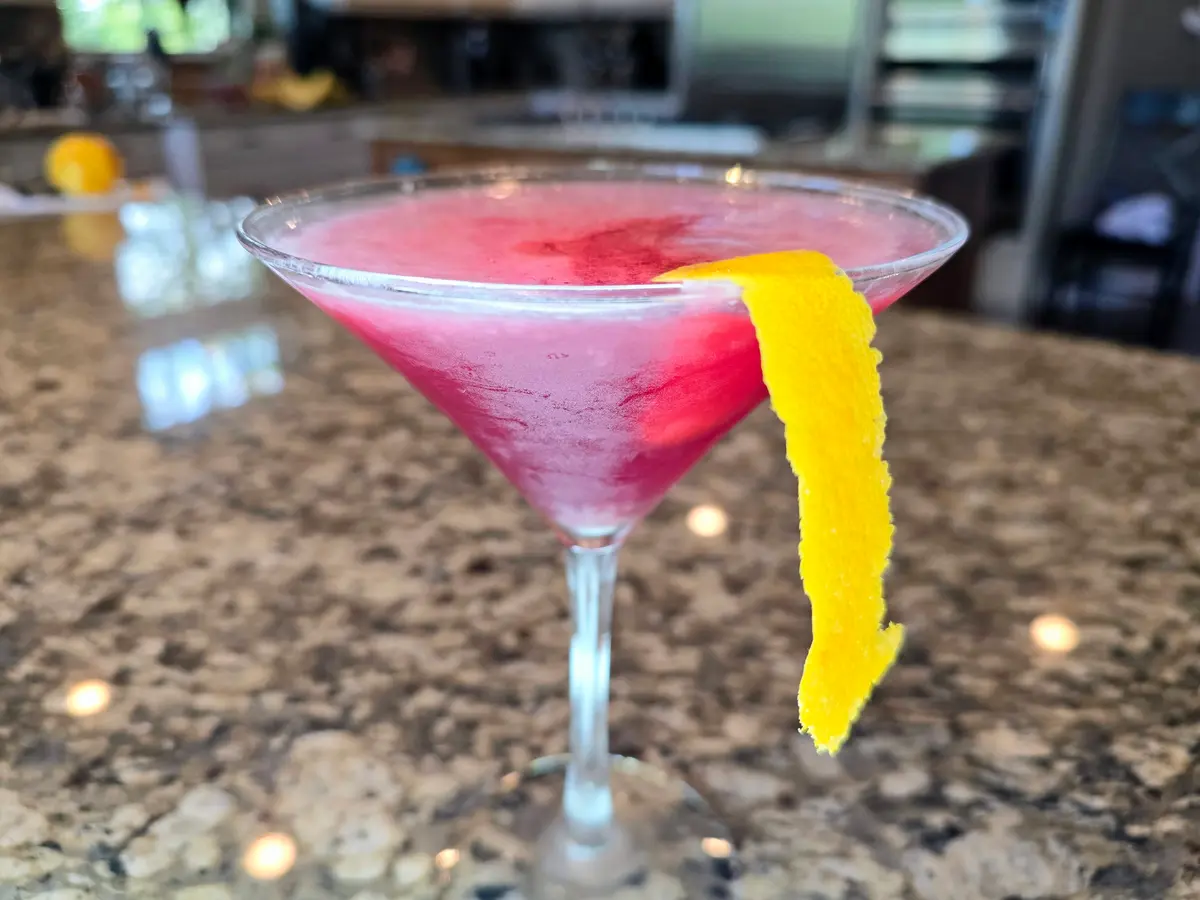 Cosmopolitan cocktail in a coupe glass with cranberry-pink color and orange spiral garnish