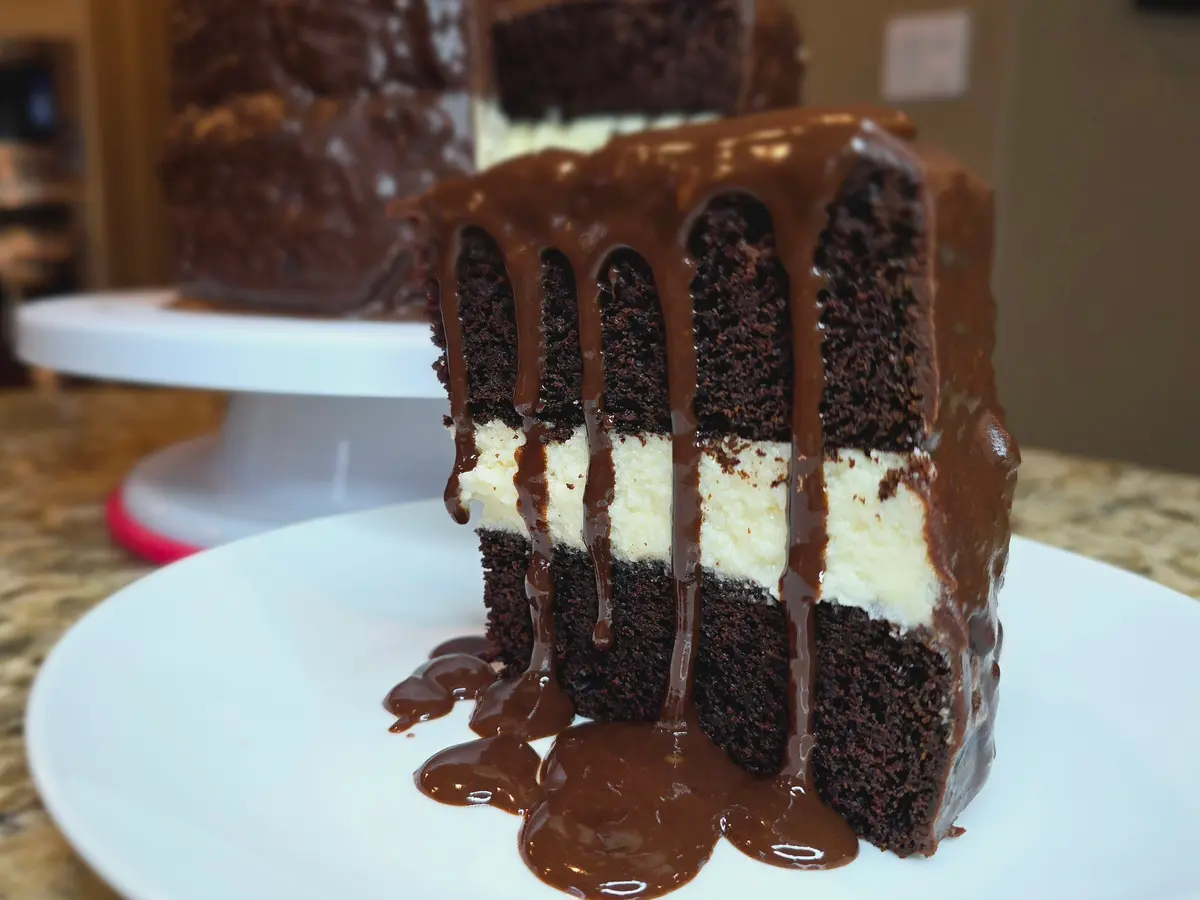Slice of homemade Ding Dong cake with dark chocolate layers, cream filling, and chocolate coating on a plate