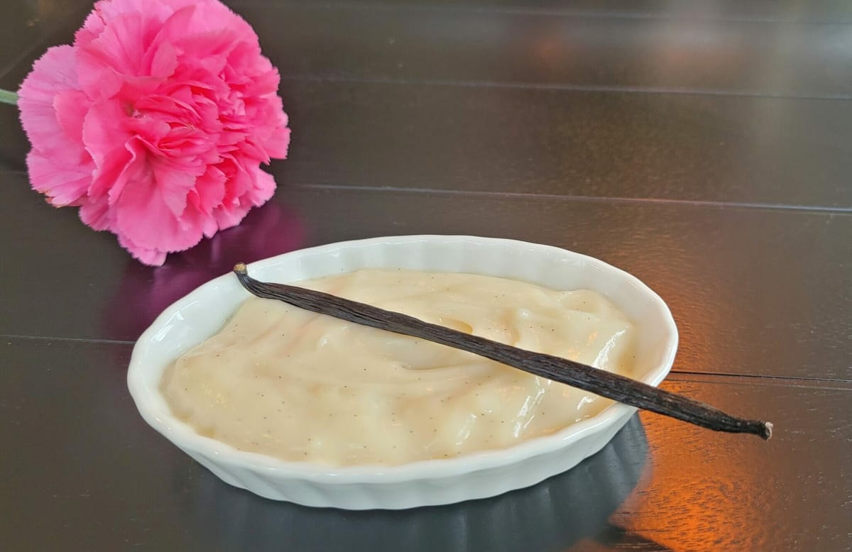 Creamy vanilla pudding in a white bowl, garnished with vanilla bean specks and fresh whipped cream