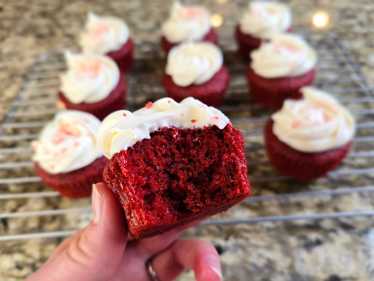 Elegant red velvet cupcakes with white chocolate cream cheese frosting and orange zest garnish on a light background