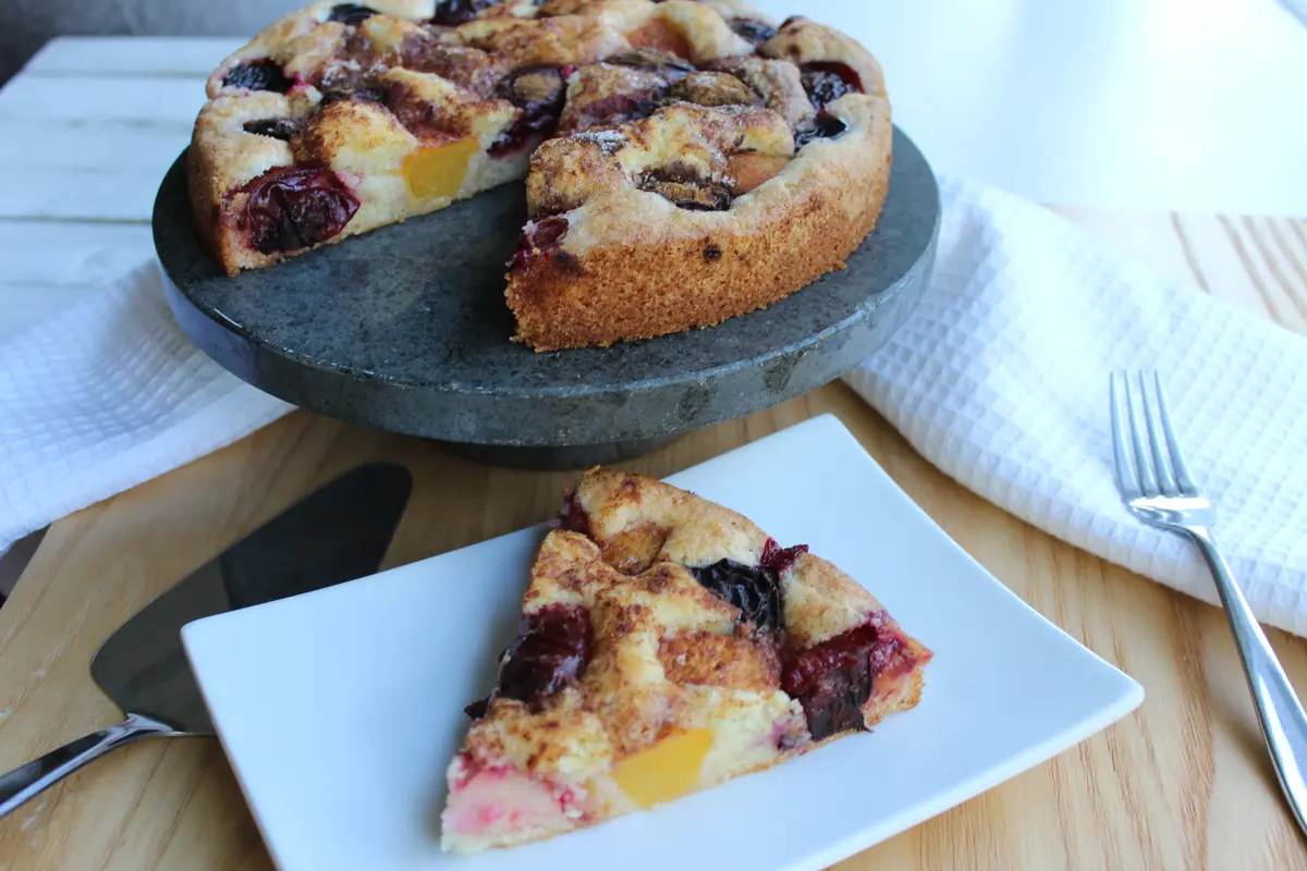 Golden-brown plum torte with fresh purple plums and crumb topping on a round cake pan