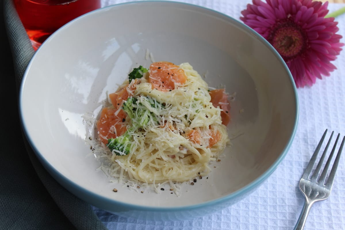 Creamy fettuccine Alfredo with smoked salmon and fresh broccoli florets on a white plate
