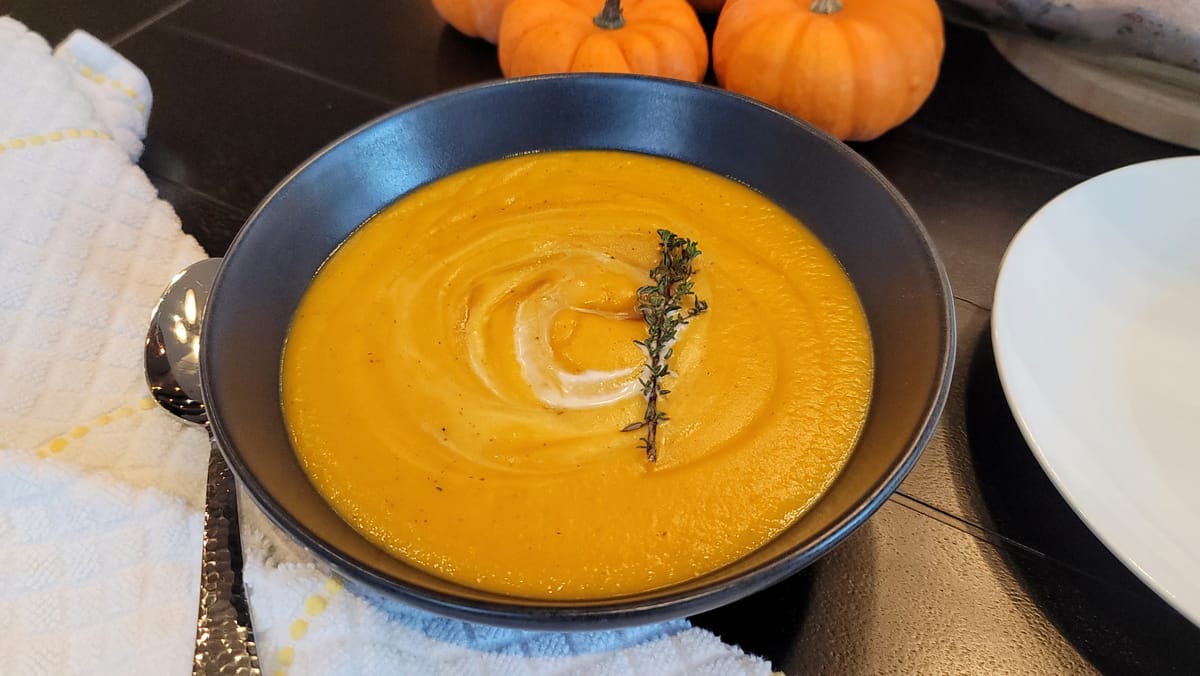 Creamy butternut squash soup in a white bowl topped with toasted pistachios, brown butter drizzle, and fresh herbs