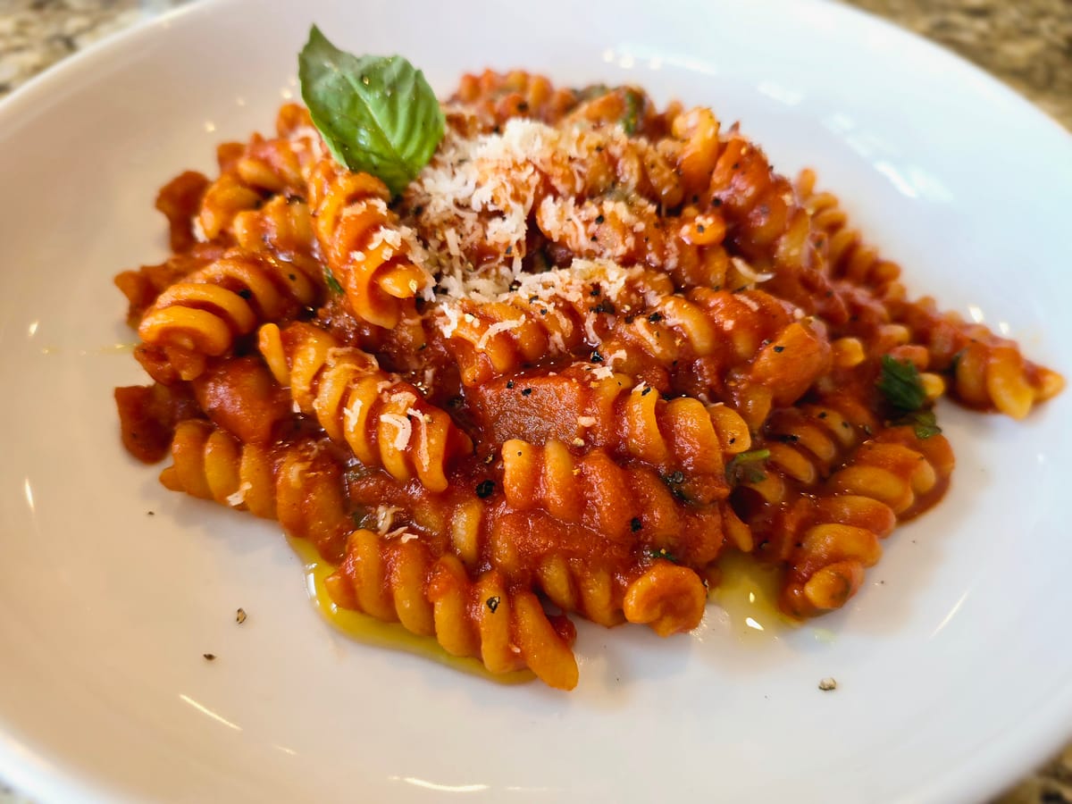 A plate of pasta al pomodoro topped with fresh basil, grated Parmesan cheese, and vibrant red tomato sauce