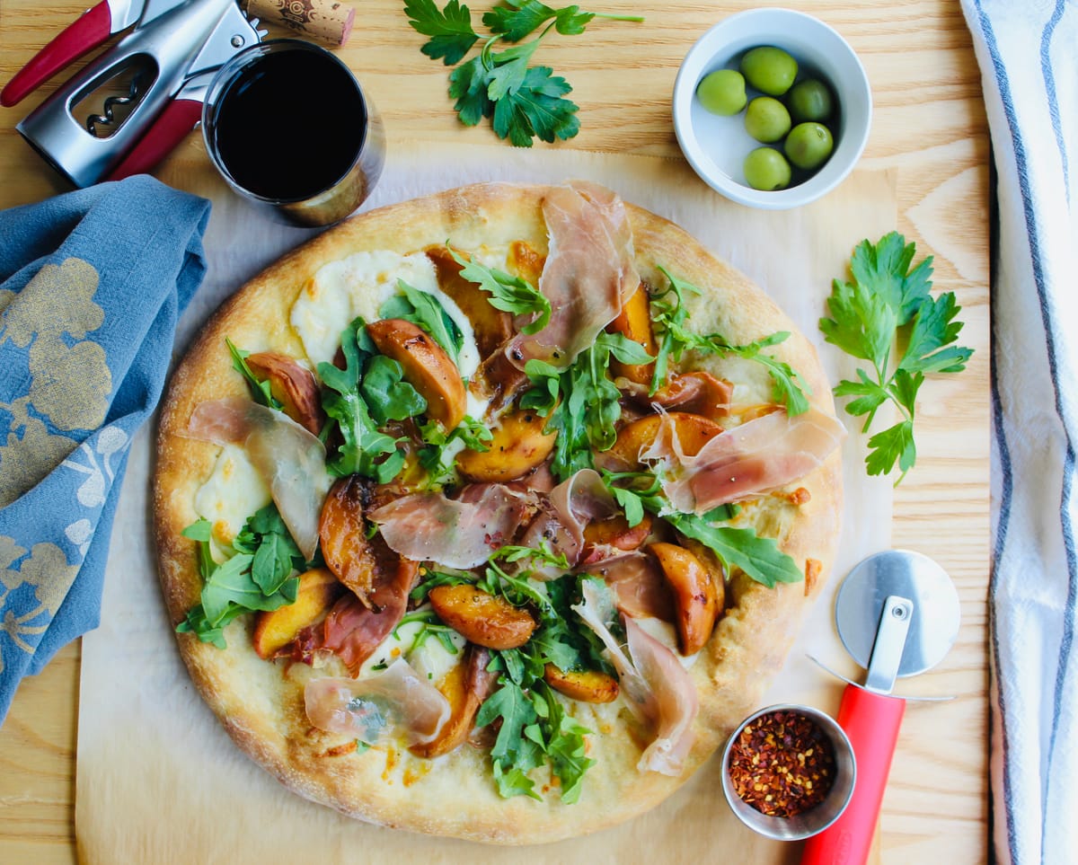 Fresh peach, prosciutto and mozzarella pizza on a wooden board with melted cheese and ripe peach slices