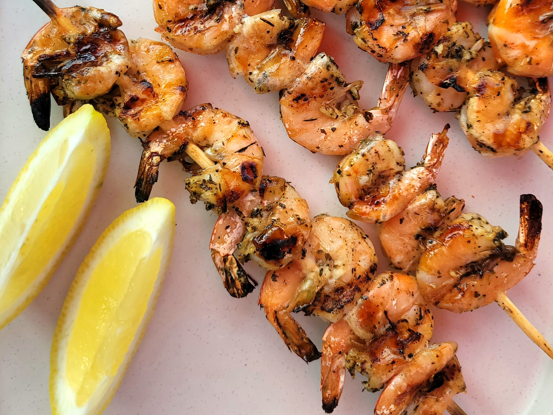 Grilled shrimp skewers with golden-brown shells on metal skewers, garnished with fresh basil and lemon