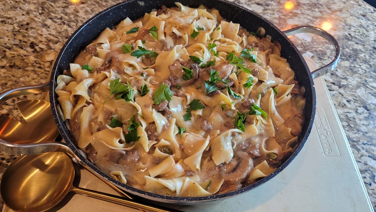 Creamy ground beef stroganoff with mushrooms and onions served over egg noodles on a white plate
