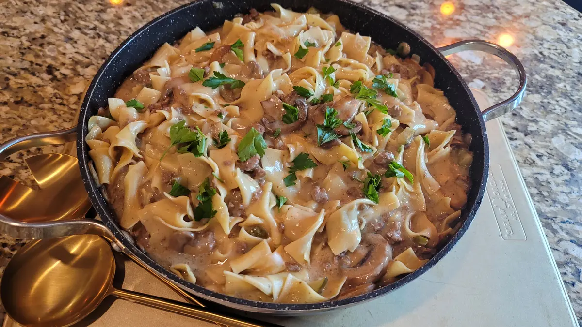 Creamy ground beef stroganoff with mushrooms and onions served over egg noodles on a white plate