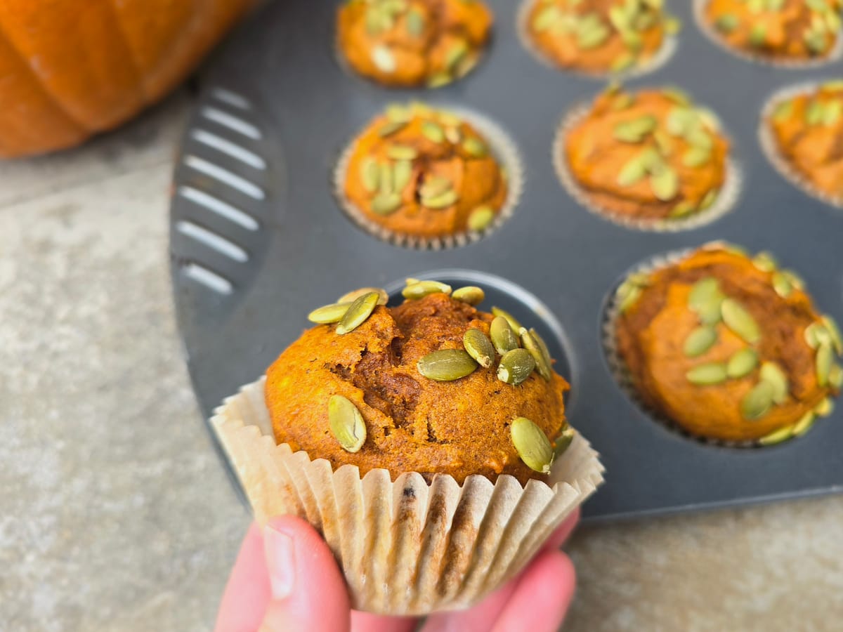 Golden-brown pumpkin cranberry muffins with tart cranberries visible on top, displayed on a white surface with autumn leaves
