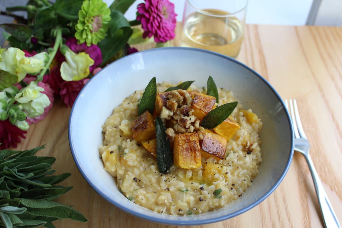 Creamy brown rice butternut squash risotto in a white bowl, garnished with sage and pumpkin seeds, with golden butternut squash cubes visible