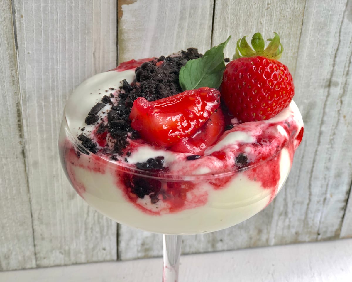 Individual berry trifle in a glass with layers of fresh strawberries, raspberries, whipped cream, and crunchy granola topping
