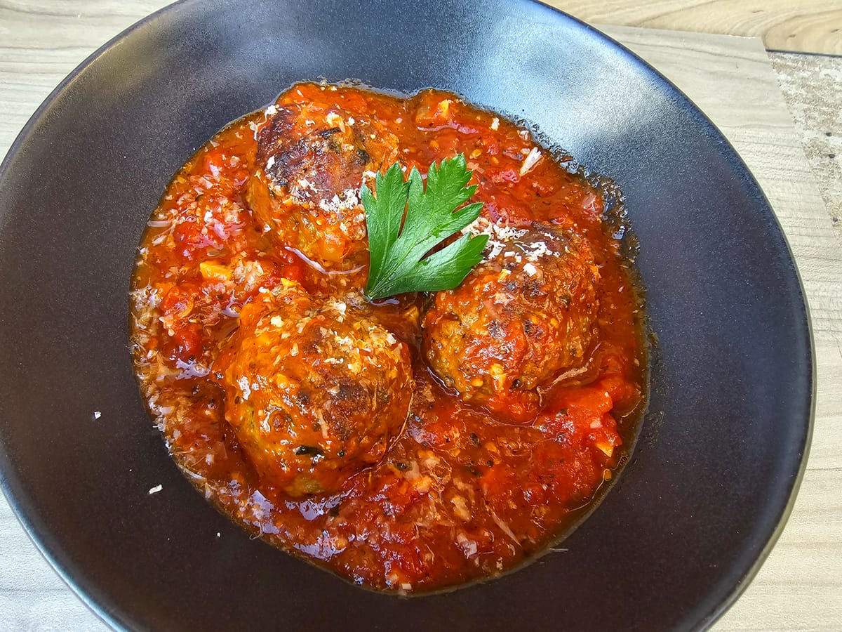 Golden-brown tender Italian meatballs stacked on a white plate with fresh parsley garnish