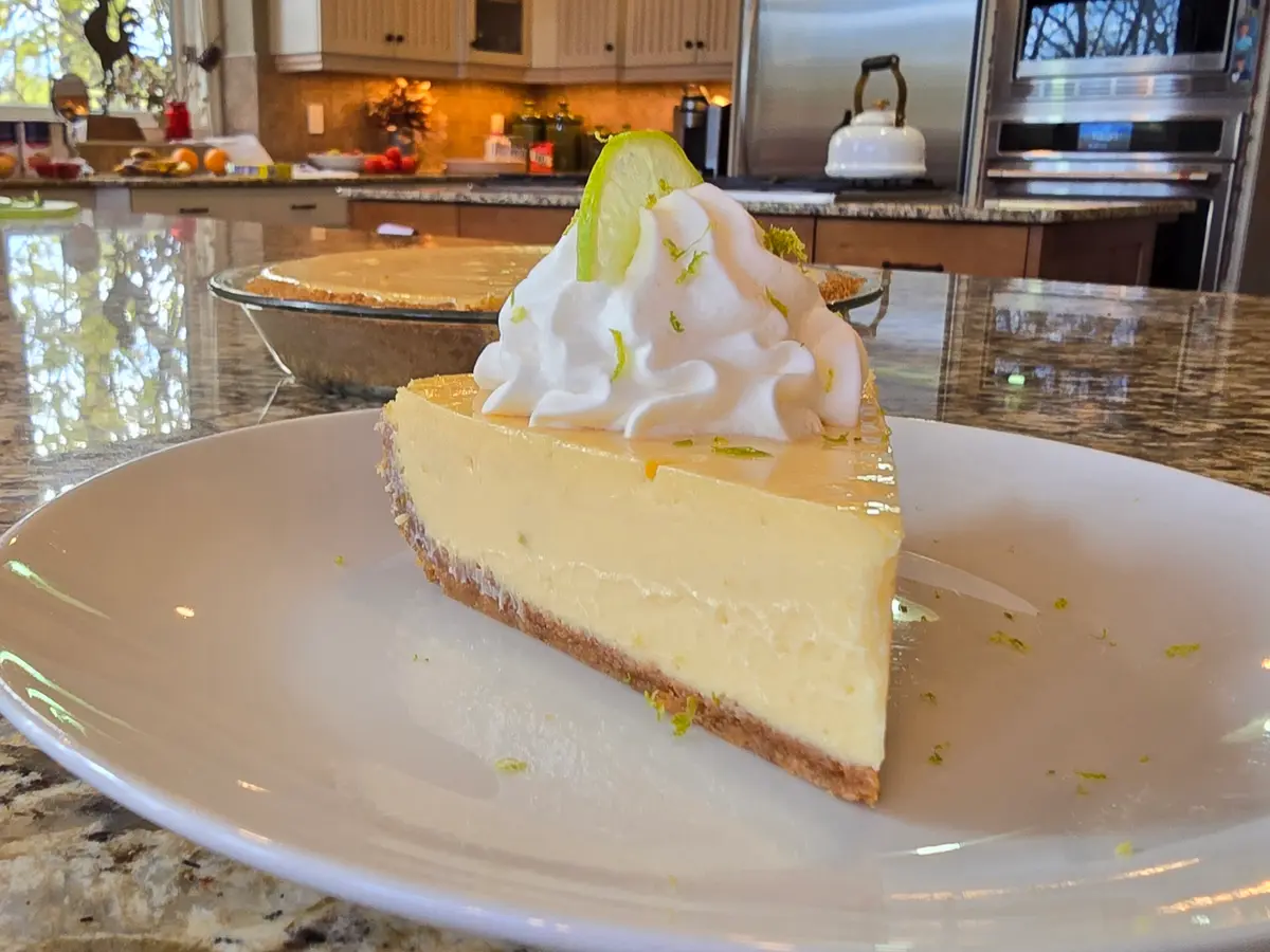 Slice of silky key lime pie with graham cracker crust and lime zest garnish on white plate