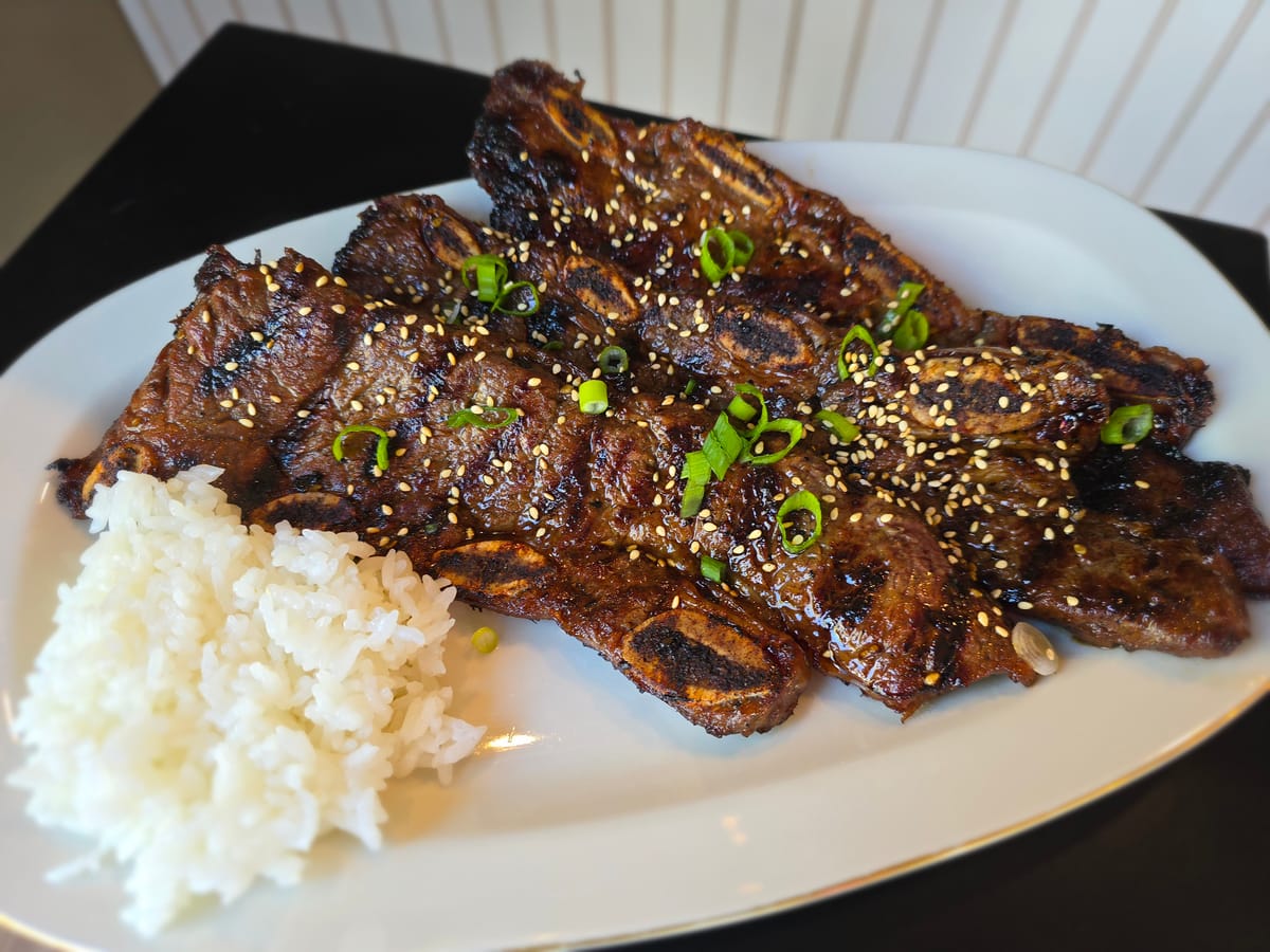 Charred Korean BBQ short ribs on a white plate with sesame seeds and fresh scallions, restaurant-style plating